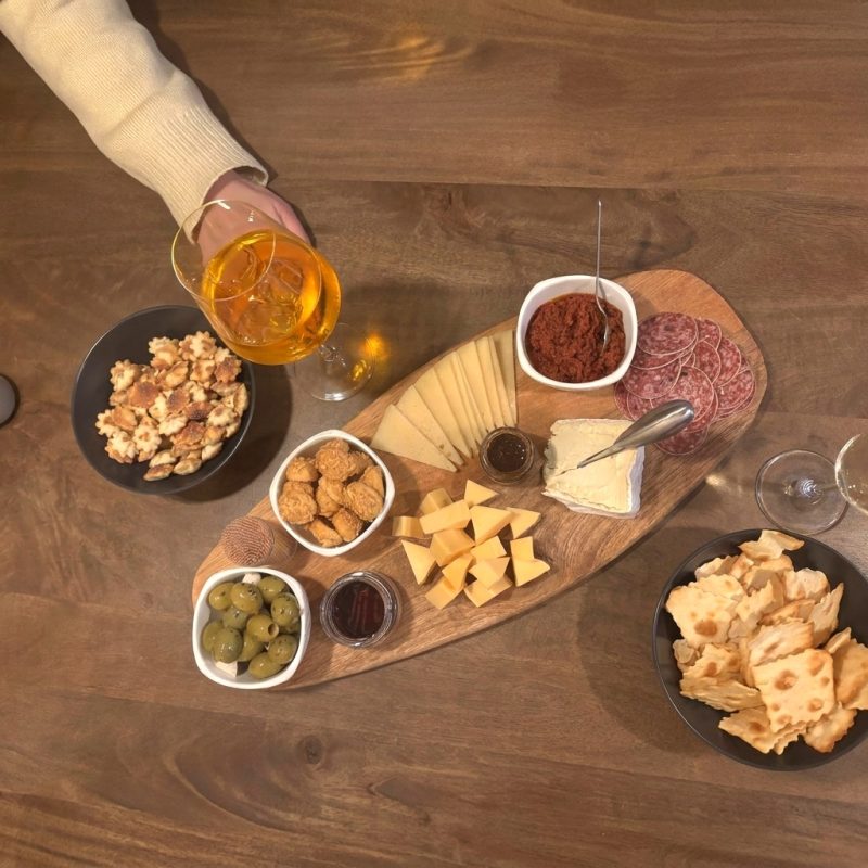 Borrelplank met diverse kazen, salami, olijven, walnoten, crackers en zongedroogde tomatentapenade, geserveerd met een Aperol Spritz