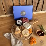 Kaasplank met Cheese In A Box doos, vier ambachtelijke kazen, druiven, walnoten en honing op houten tafel