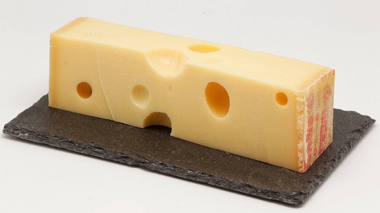 Stuk Emmentaler kaas met grote ronde gaten op een leisteen plank
