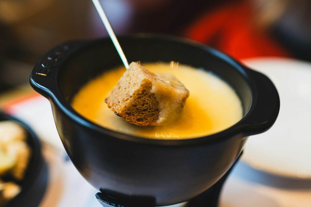 Stuk stokbrood wordt uit een pan gesmolten bergkaas getrokken met lange goudgele kaasdraden