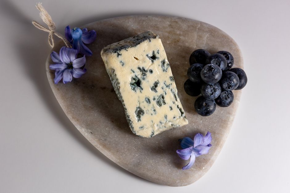 Punt blauwaderkaas met blauwe aders op een stenen plank met druiven, een klassiek beeld van Roquefort of Stilton